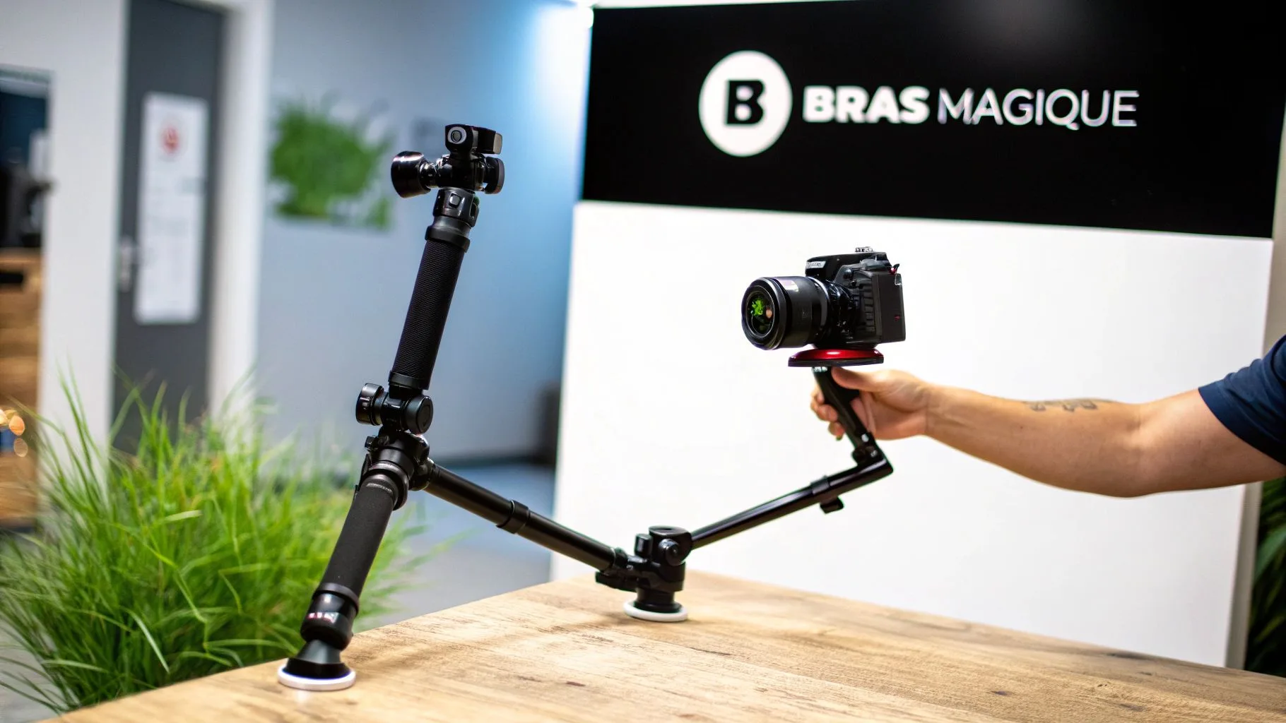 Deux bras magiques noirs supportant une caméra et fixés à une table en bois, devant un logo Bras Magique.